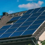 Ein Hausdach mit dunklen Dachpfannen, das großflächig mit modernen, dunkelblauen Photovoltaik-Modulen belegt ist.